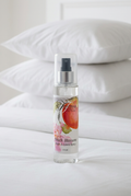Peach Blossom Room & Linen Spray standing upright on a white bed with stacked white pillows.